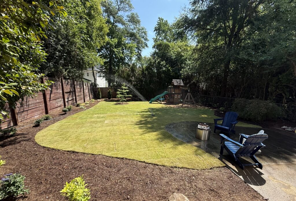 After – wide backyard shot: New sod lawn and mulch beds in a Raleigh, NC backyard, with patio seating and play area in the background